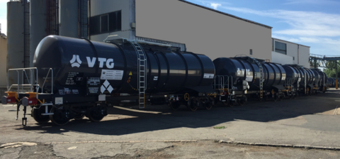 Black tank car in front of gray hall