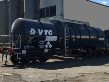 Black tank car in front of gray hall