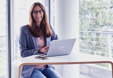 Lachende VTG-Mitarbeiterin an Tisch mit Laptop